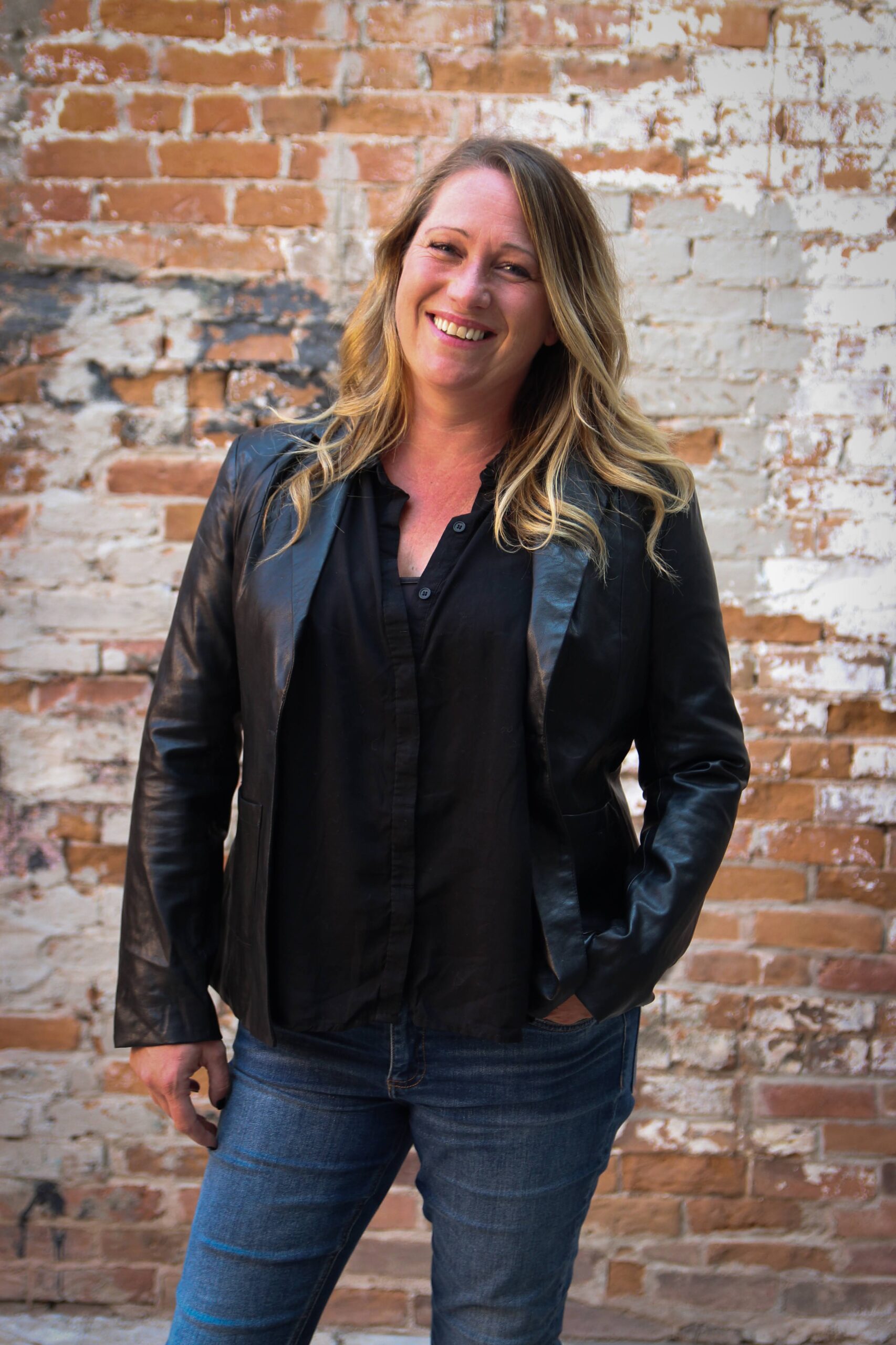 A photographic portrait of Ruth Lorensson smiling and standing outside in front of a mottled brick wall